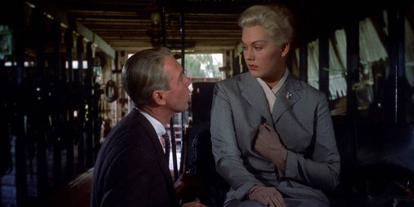 Scottie, played by Jimmy Stewart, kneeling next to a sitting Judy, played by Kim Novak, with Judy wearing a matching gray jacket and skirt, in Vertigo