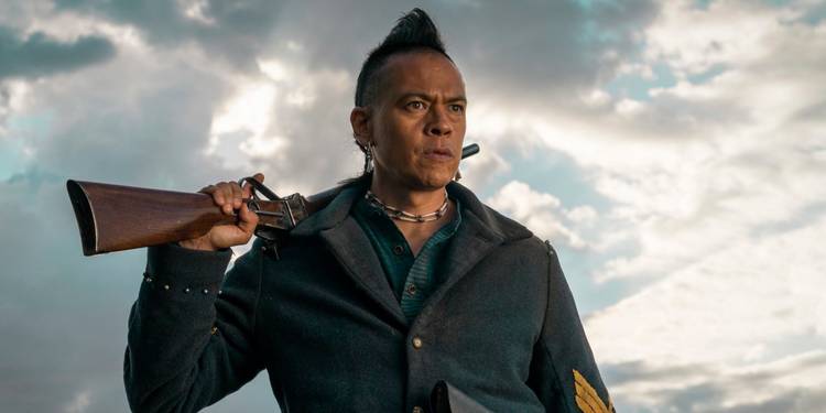 Chaske Spencer holding a rifle over his shoulders in The English