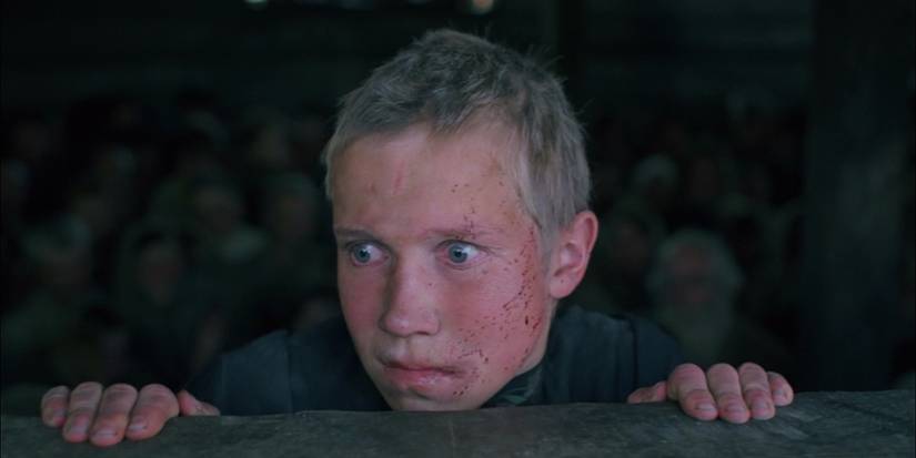 Aleksei Kravchenko as Flyora Gaishun, holding onto a window ledge and looking horrified, with a crowd of people behind him in Come and See