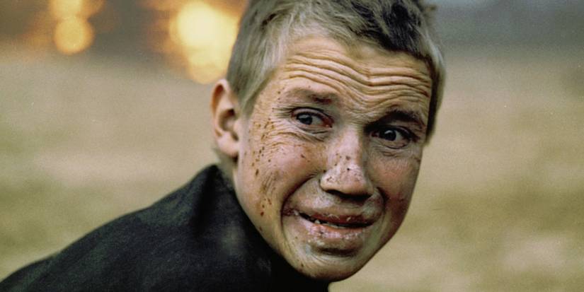 Aleksei Kravchenko as Flyora Gaishun, standing in front of a fire looking devastated in Come and See.