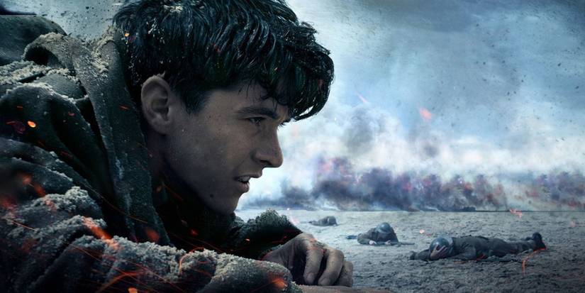 Tommy crawling on a beach surrounded by smoke and other soldiers in Dunkirk