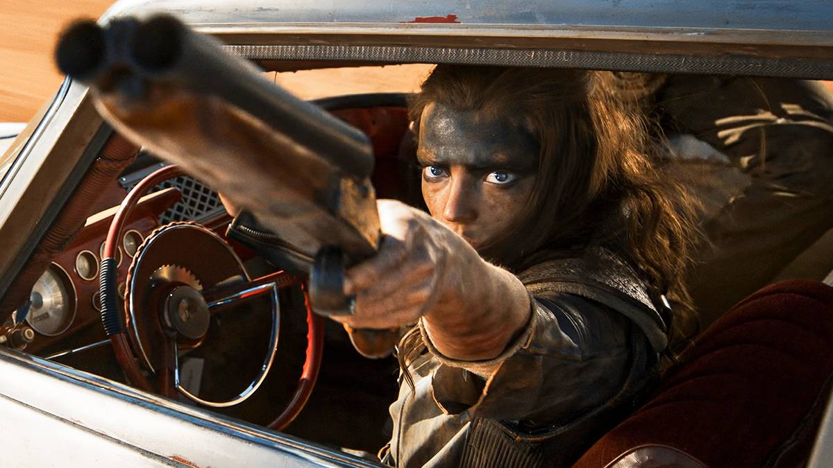 Furiosa driving a car while aiming a gun at someone off-camera in Furiosa: A Mad Max Saga