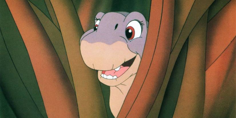 Littlefoot (voiced by Gabriel Damon) peering out from tall grass and smiling in The Land Before Time