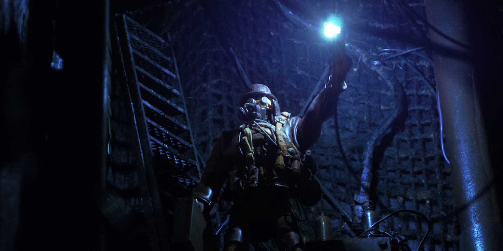 A masked figure standing in a dark room holding up a light in Mad God - 2021