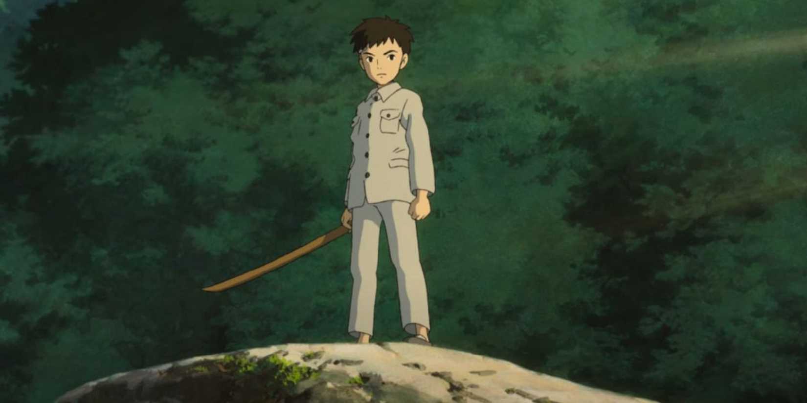 Mahito standing atop a hill holding a stick in The Boy and the Heron