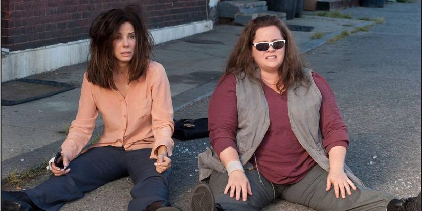Melissa McCarthy dan Sandra Bullock menyaksikan ledakan saat mereka duduk di tanah di The Heat.