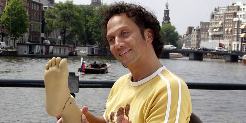 Rob Schneider as Deuce Bigalow holding a prosthetic foot in Deuce Bigalow: European Gigolo