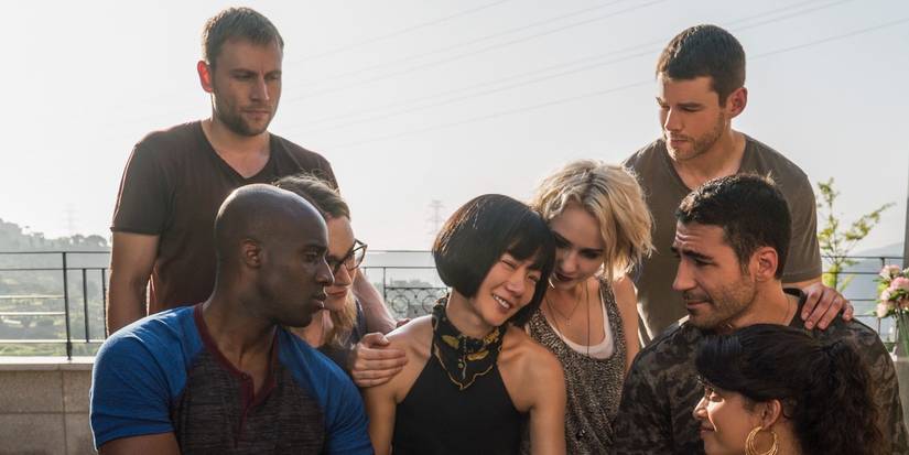 The cast of Sense 8 huddle around Bae Doona on a rooftop balcony.