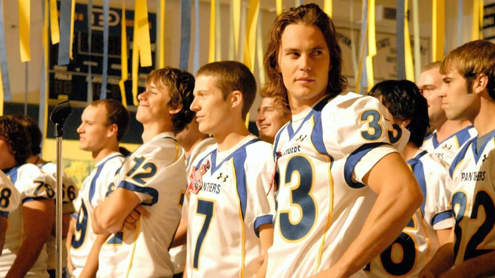 Taylor Kitsch as Tim Riggins and Zach Gilford as Matt Saracen wearing football jerseys in Friday Night Lights.