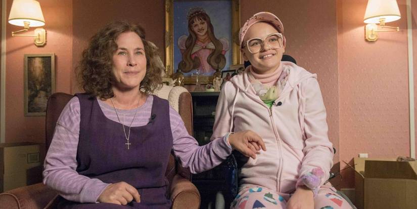 Patricia Arquette next to Joey King in a wheelchair holding hands as they smile at the camera in The Act.
