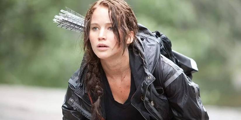 Jennifer Lawrence as Katniss Everdeen looks into the distance while crouching in The Hunger Games.