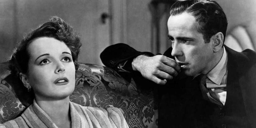 Mary Astor leaning back on a couch with Humphrey Bogart sitting close and watching her in The Maltese Falcon