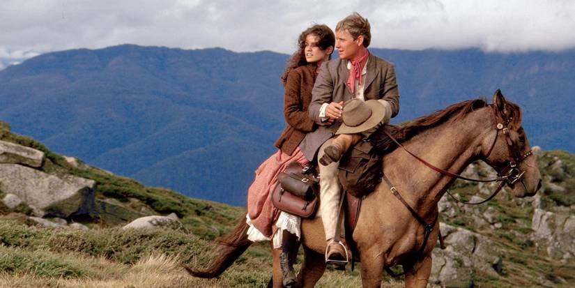 Jim Craig (Tom Burlinson) and Jessica Harrison (Sigrid Thornton) sit on horseback in the Australian wilderness.