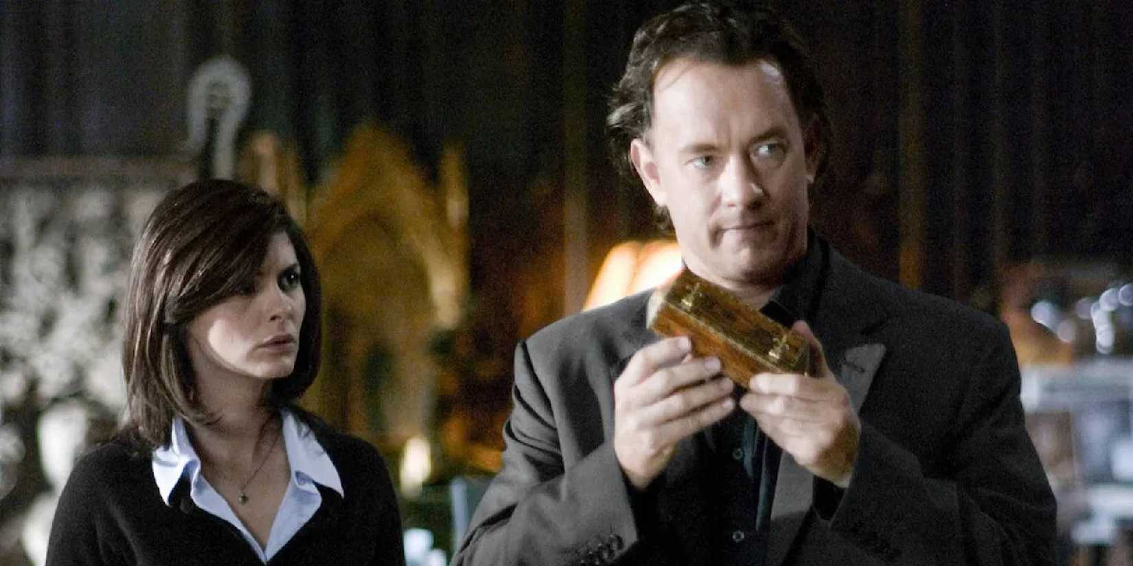 Tom Hanks and Audrey Tautou in The Da Vinci Code stand side by side and look at a cylinder lockbox.