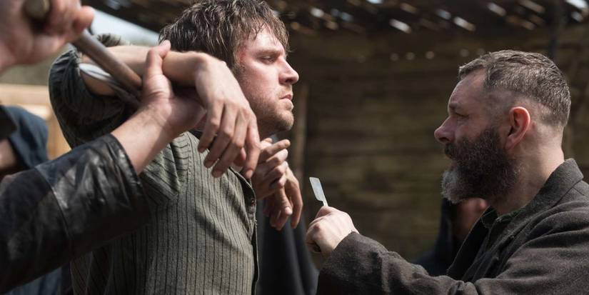 Dan Stevens being restrained in front of Michael Sheen threatening him with a straight razor in Apostle.