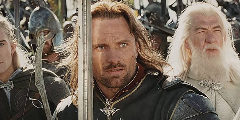 Aragorn (Viggo Mortensen), holds his sword close to his face as a light shines across him. He is surrounded by allied soldiers, along with Legolas and Gandalf