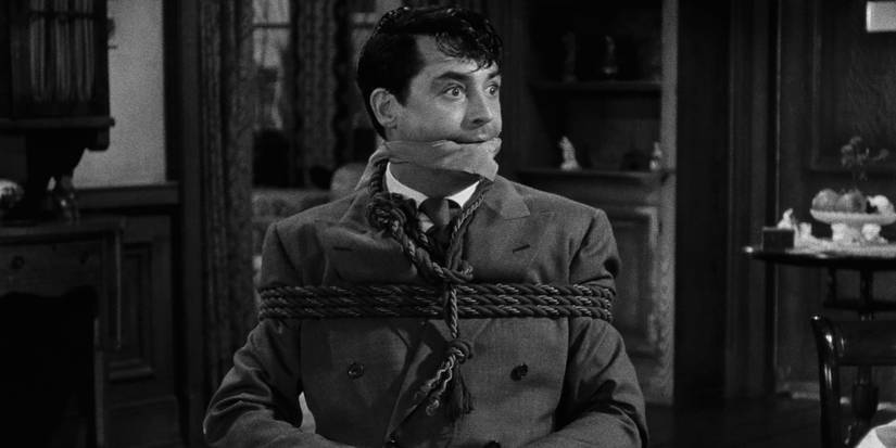 Mortimer Brewster (Cary Grant) sits gagged and tied to a chair in the middle of a large living area in 'Arsenic and Old Lace' (1944)