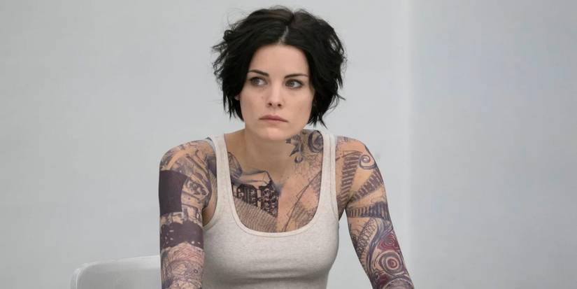A heavily tattooed woman, Jane Doe (Jamie Alexander), wears a singlet as she sits in an FBI interrogation room waiting to be questioned in 'Blindspot' (2015-2020)