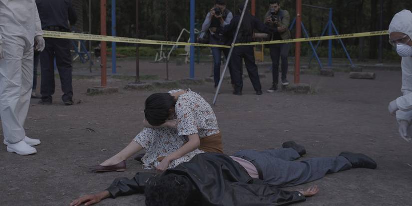 A woman sits beside a dead man, covering her face in Disappear Completely