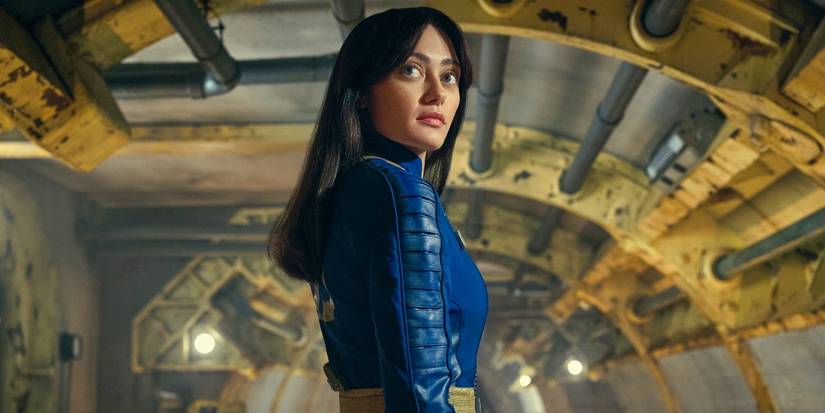Lucy standing in a Vault looking over her shoulder toward the camera in Fallout.