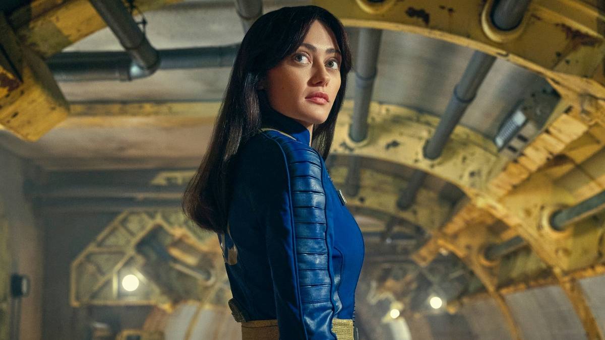 Lucy standing in a Vault looking over her shoulder toward the camera in Fallout.