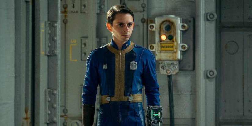 Moises Arias in a blue and yellow jumpsuit looking angry in Fallout Season 1.
