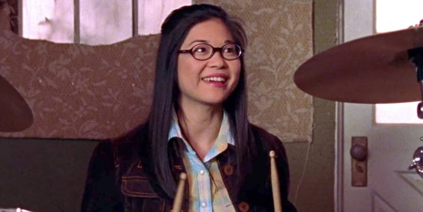 Keiko Agena as Lane Kim, sitting at her drum set, holding drumsticks, and smiling on Gilmore Girls