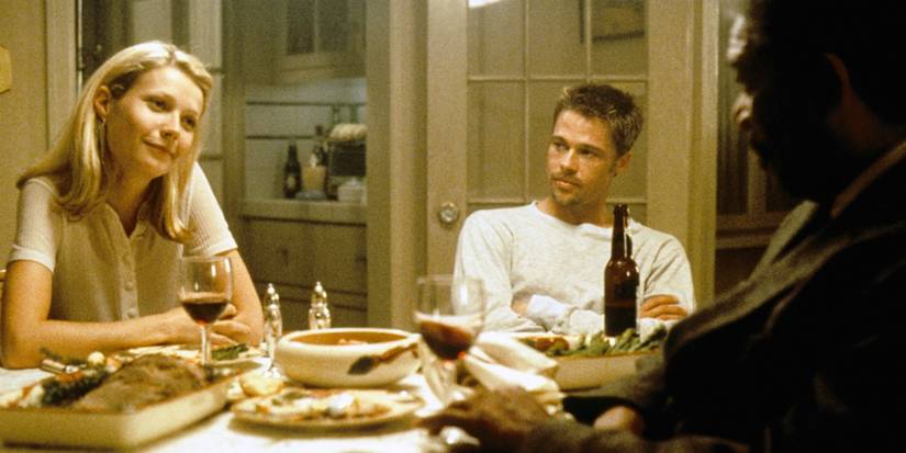 Gwyneth Paltrow sitting at a dinner table with Brad Pitt and Morgan Freeman in Seven.