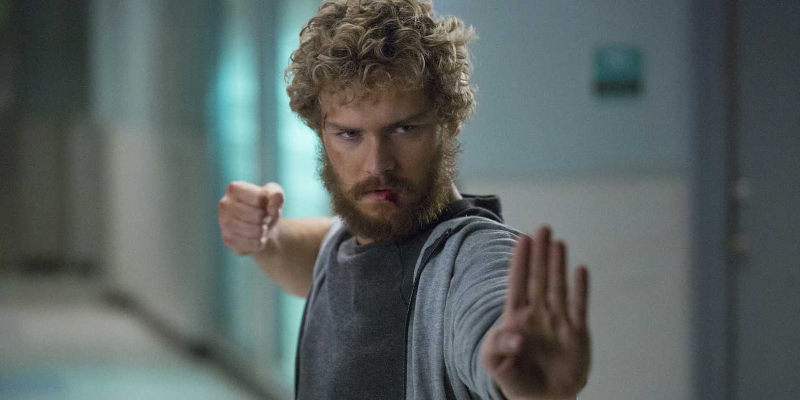 Danny Rand in a hallway with a scruffy beard and blood on his lip gets into a fighting stance in Iron Fist.