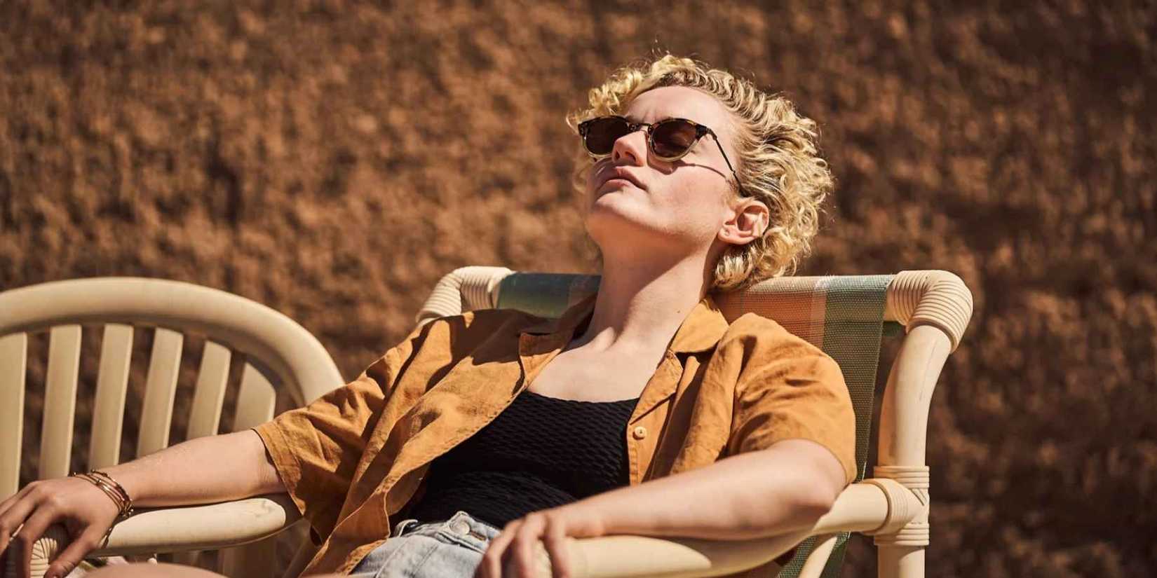 Julia Garner as Hanna, lounging on a chair in the sun, in The Royal Hotel