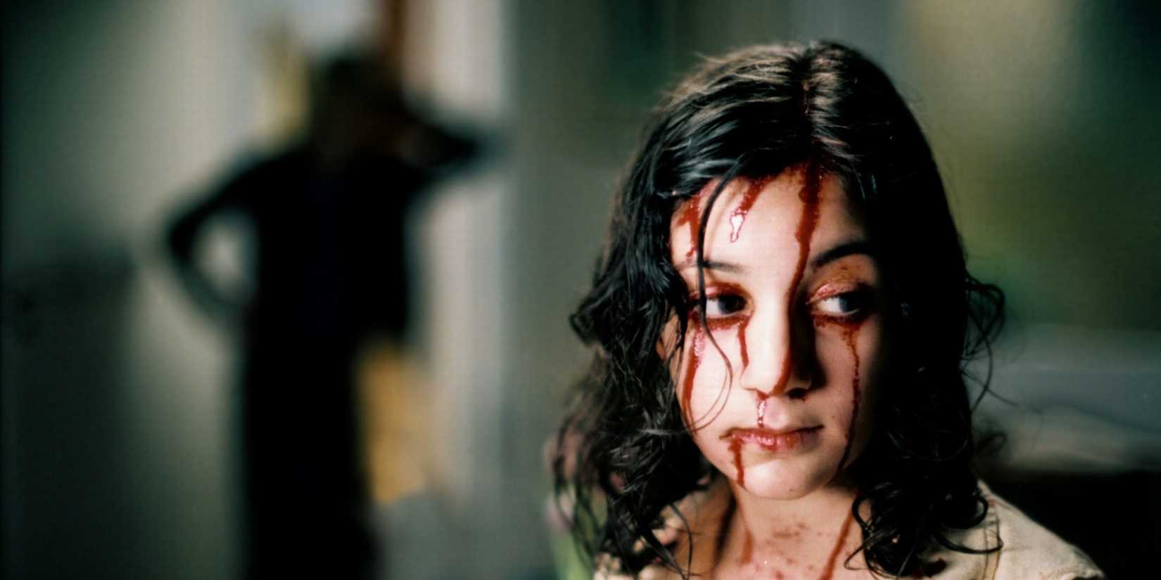 Lina Leandersson como Eli coberta de sangue em frente a uma figura sombria, deixe o certo entrar.