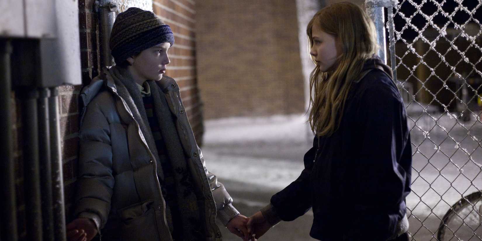 Kodi Mit-McPhee sebagai Owen dan Chloe Grace Moretz sebagai Abby berpegangan tangan di luar di Let Me In (2010)