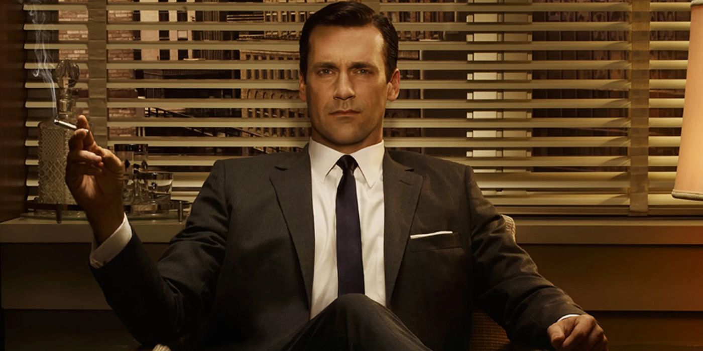 Jon Hamm as Don Draper in Mad Men sitting in a chair in his office with a cigarette in his hand.
