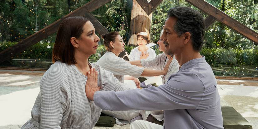 Benjamin Bratt sitting across from Maya Rudolph with his hand on her chest in Loot