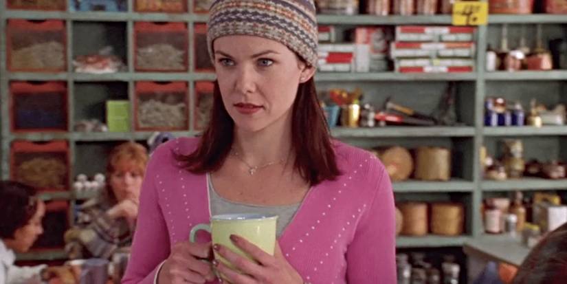 Lauren Graham as Lorelai wearing a hat & holding a coffee cup in Luke's Diner in the Gilmore Girls pilot.