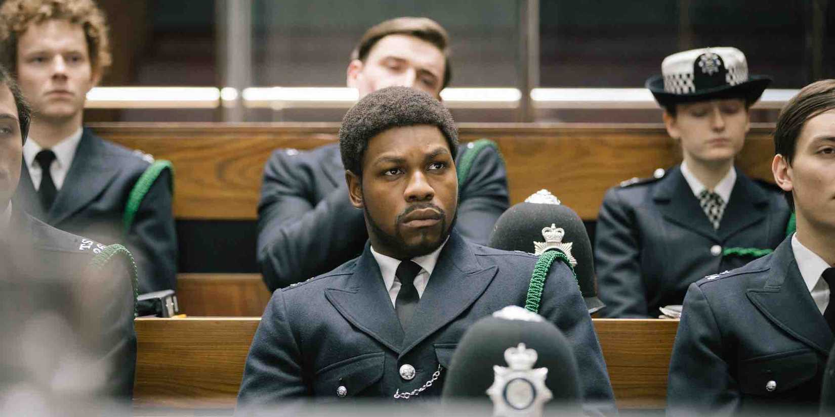 Leroy Logan sitting in a crowd of soldiers looking intently ahead Small Axe Red White and Blue