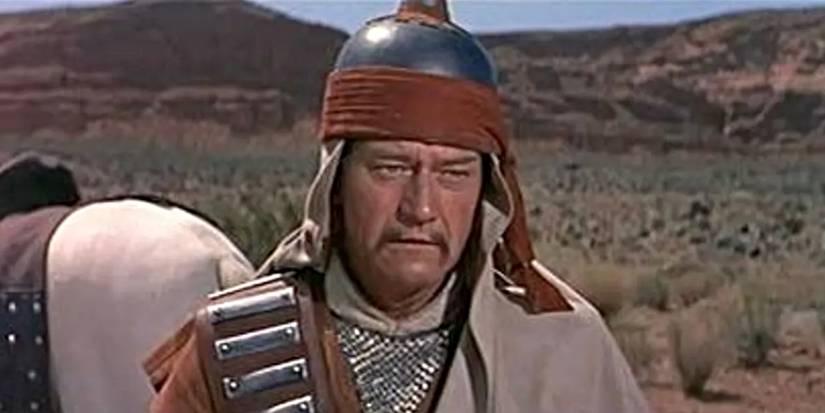 John Wayne as Genghis Khan, standing outside beside a horse in The Conqueror