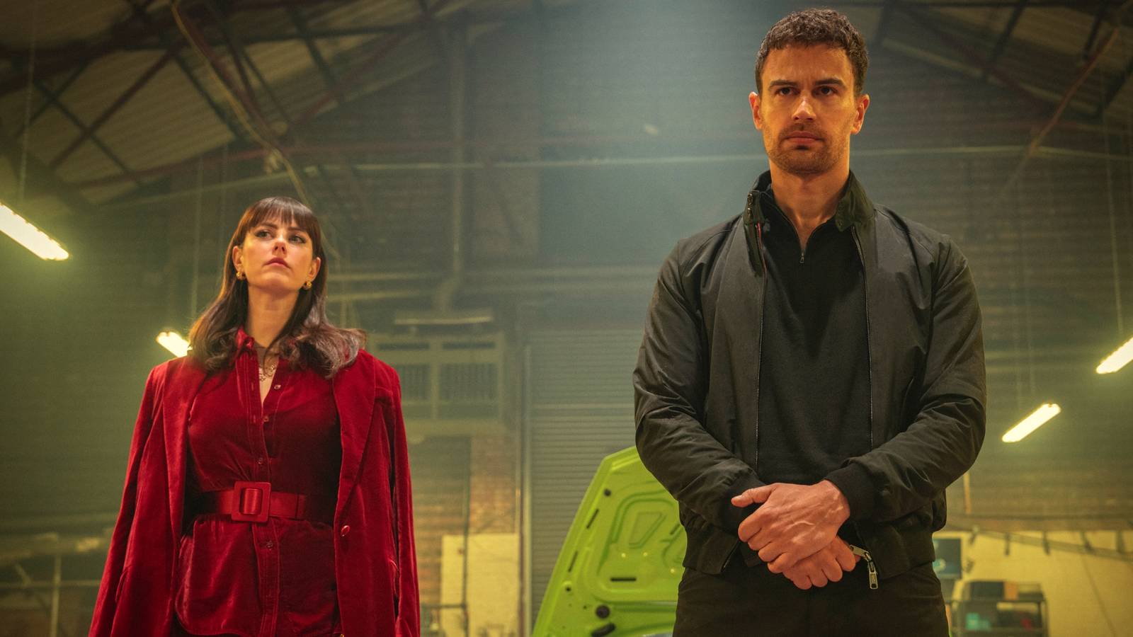 Kaya Scodelario as Susie standing with Theo James as Eddie in a warehouse in The Gentlemen