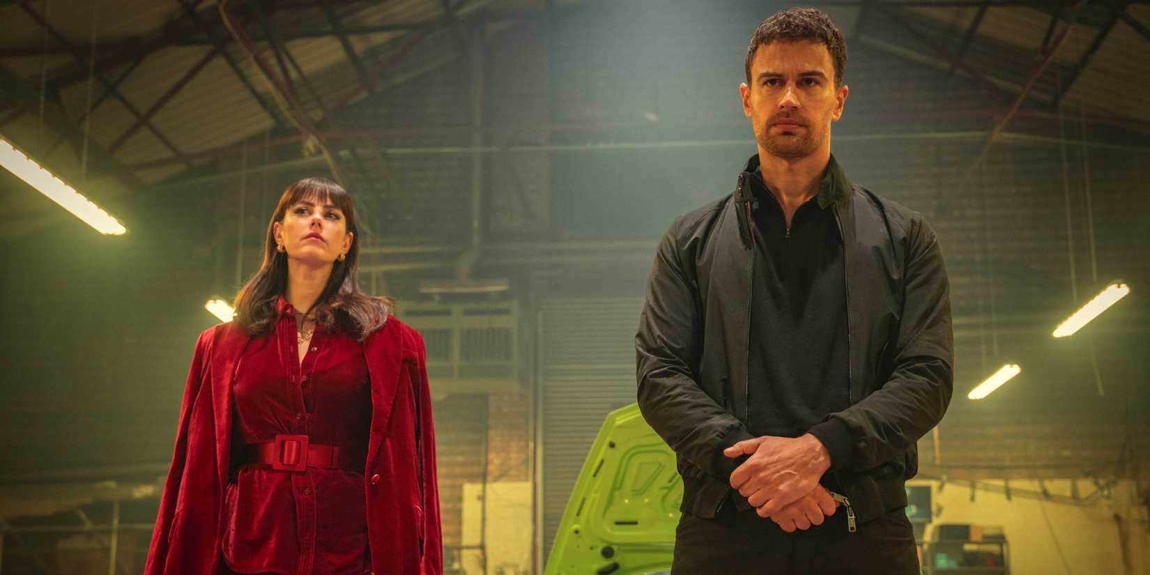 Kaya Scodelario as Susie standing with Theo James as Eddie in a warehouse in The Gentlemen