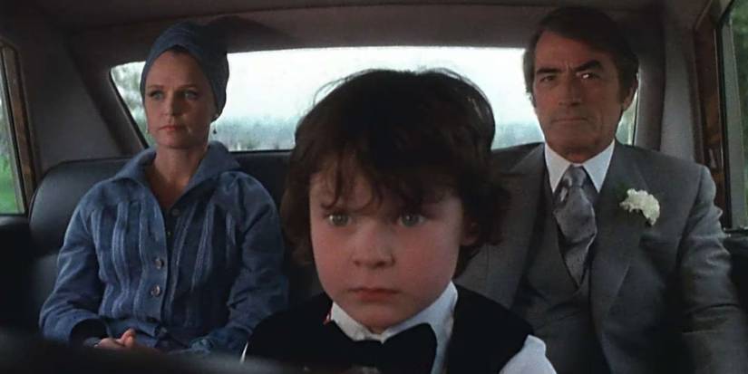 Damien (Harvey Spencer Stephens) in the foreground looking angered as Robert (Gregory Peck) and Katherine (Lee Remick) sit behind.