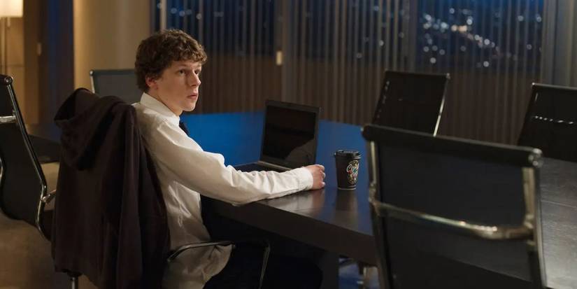 Mark Zuckerberg (Jesse Eisenberg) sits in a boardroom with a laptop in The Social Network.
