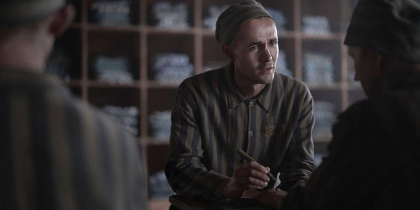 Jonah Hauer-King signing a paper while in a prison uniform.