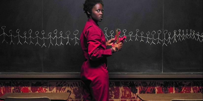 Red cuts up paper stick people while staring at a chalkboard full of stick figures in a classroom