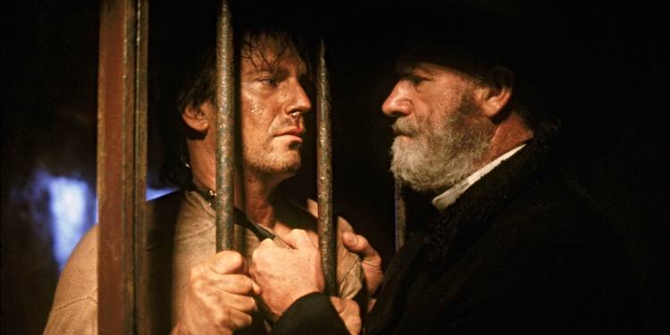 Gene Hackman as Nicholas Earp, holding Kevin Costner as Wyatt Earp by the collar through jail cell bars