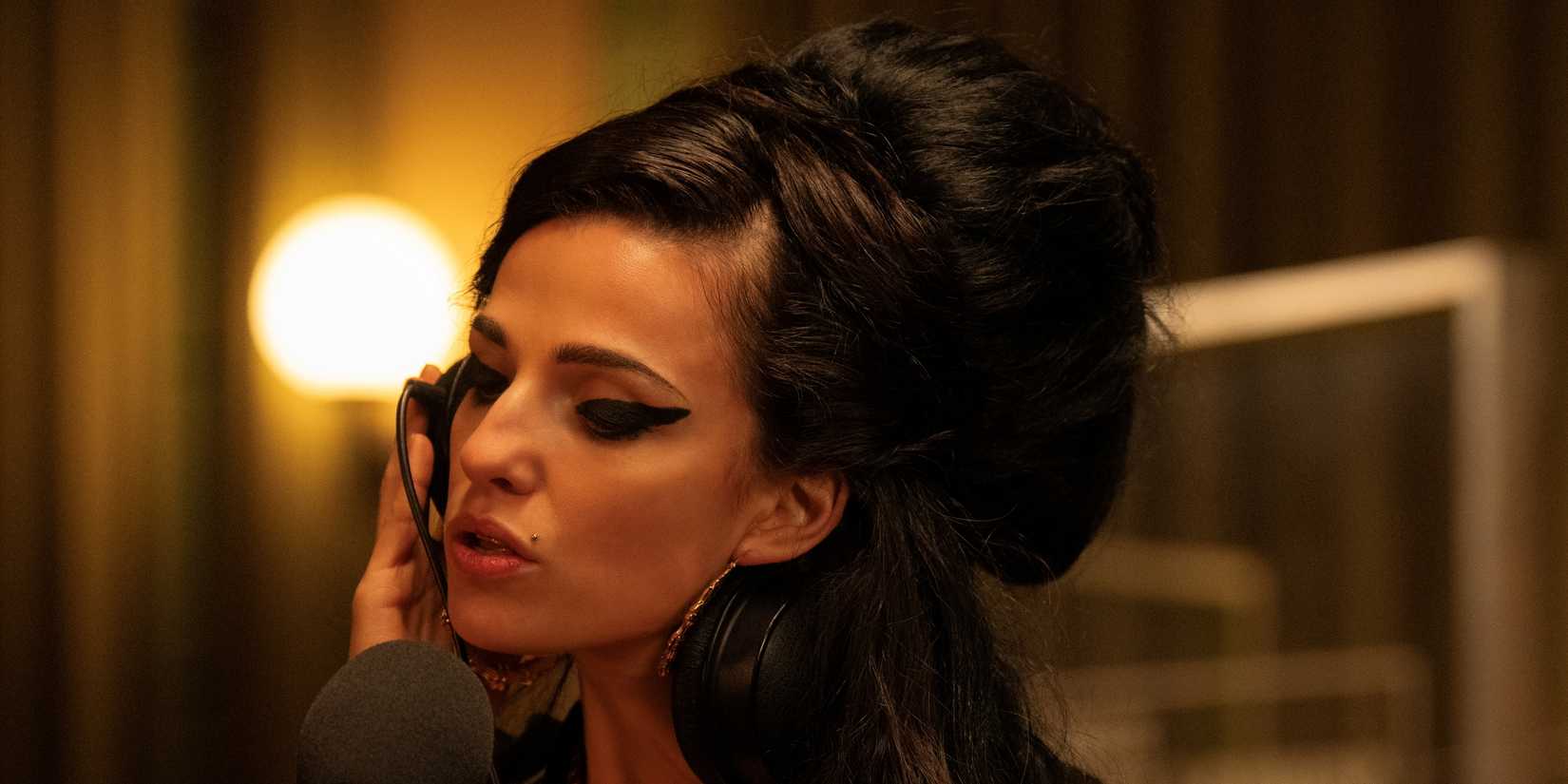 Marisa Abela sebagai Amy Winehouse memegang headphone di telinga kanannya di studio rekaman di Back to Black