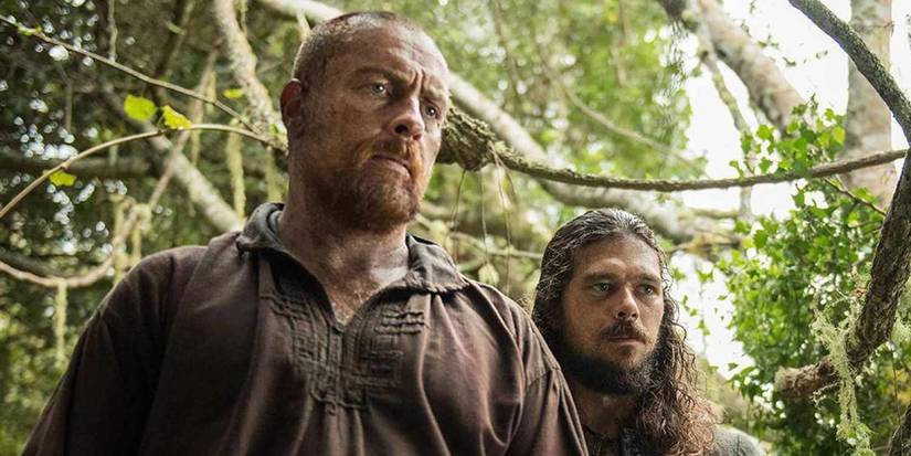 Captain Flint and John Silver in Black Sails standing next to each other in the jungle.