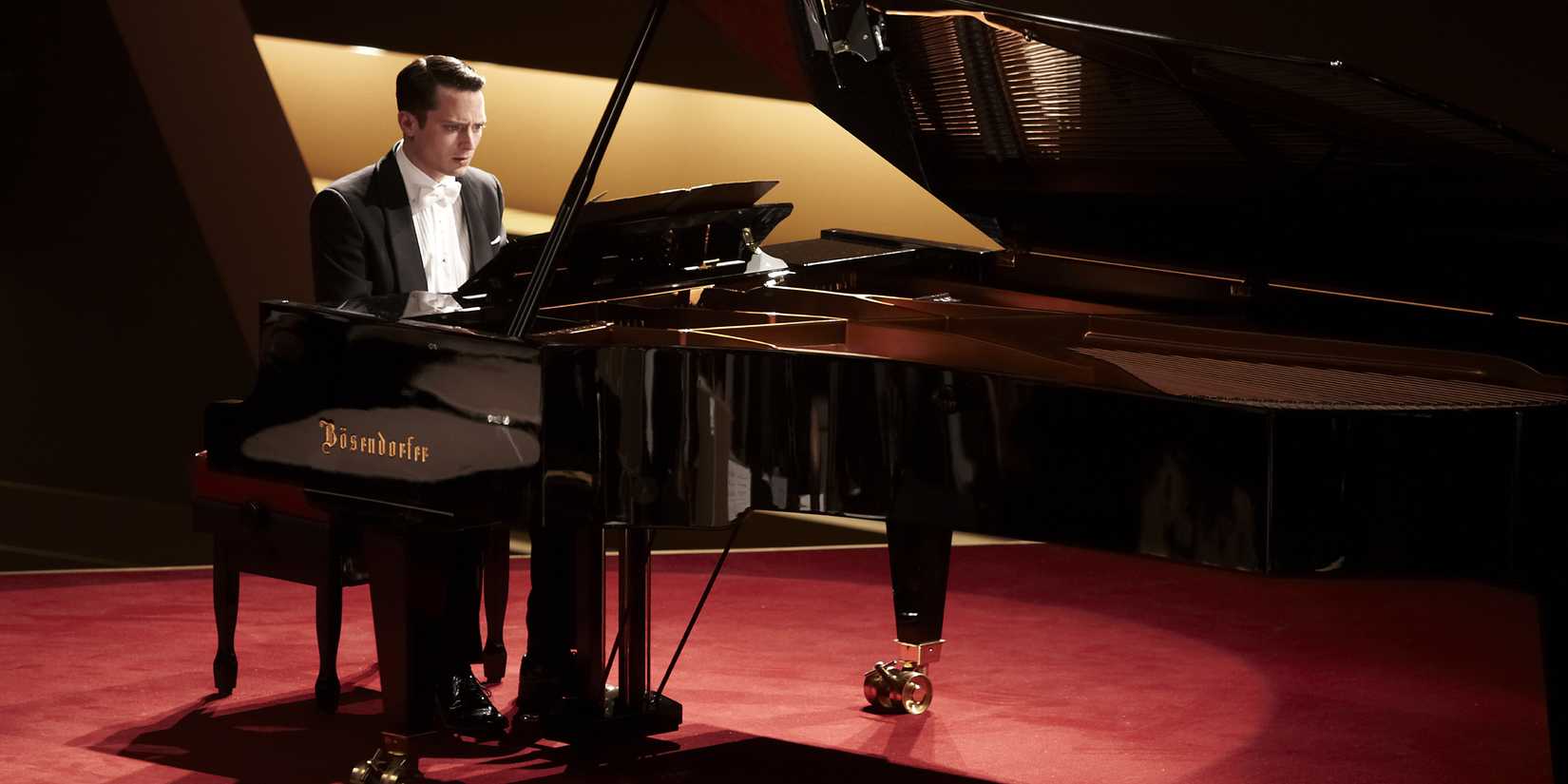A man looks worried as he plays a grand piano on a stage