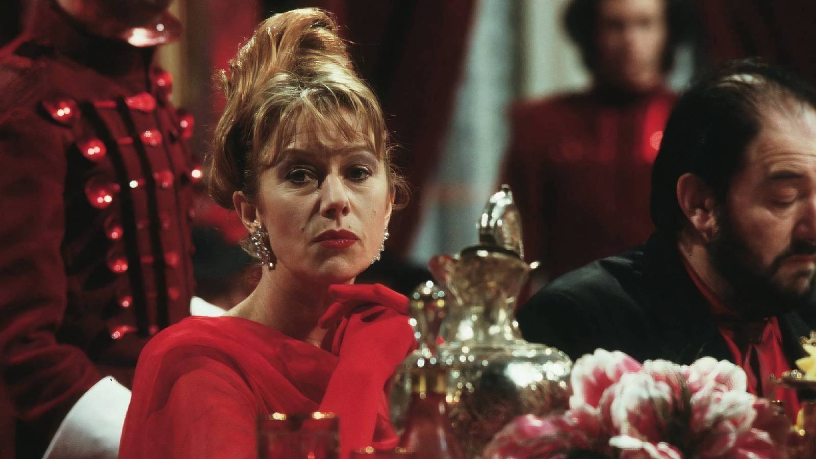 Helen Mirren as Georgina Spica sitting at a fancy dinner table in The Cook, the Thief, His Wife & Her Lover.