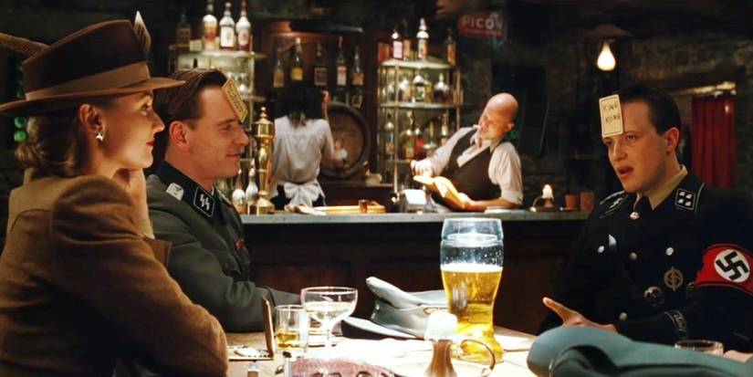 The ensemble cast of Inglorious Basterds sitting together in a tavern playing drinking games