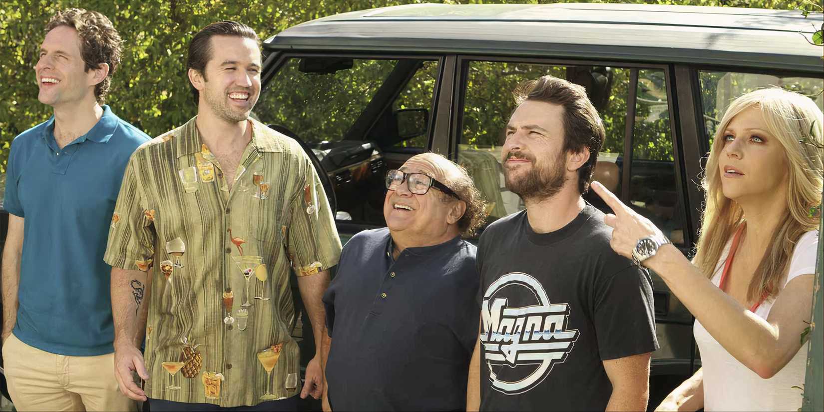 The cast of 'It's Always Sunny in Philadelphia' stand in front of a car smiling at something off-camera